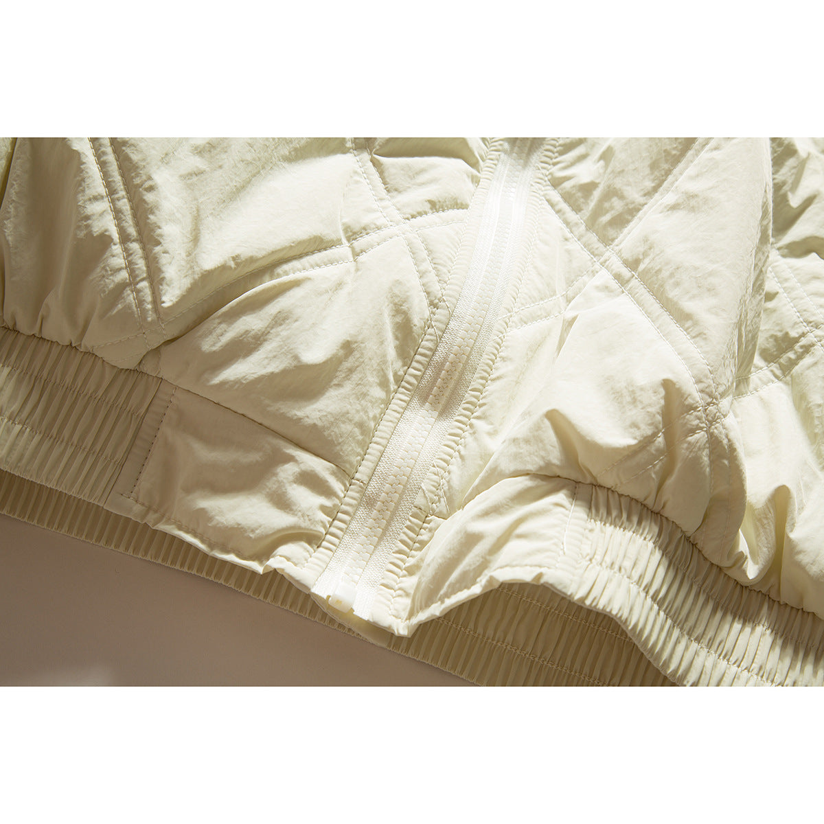 Close-up of the ivory jacket's front zipper, quilted panels, and gathered hem.