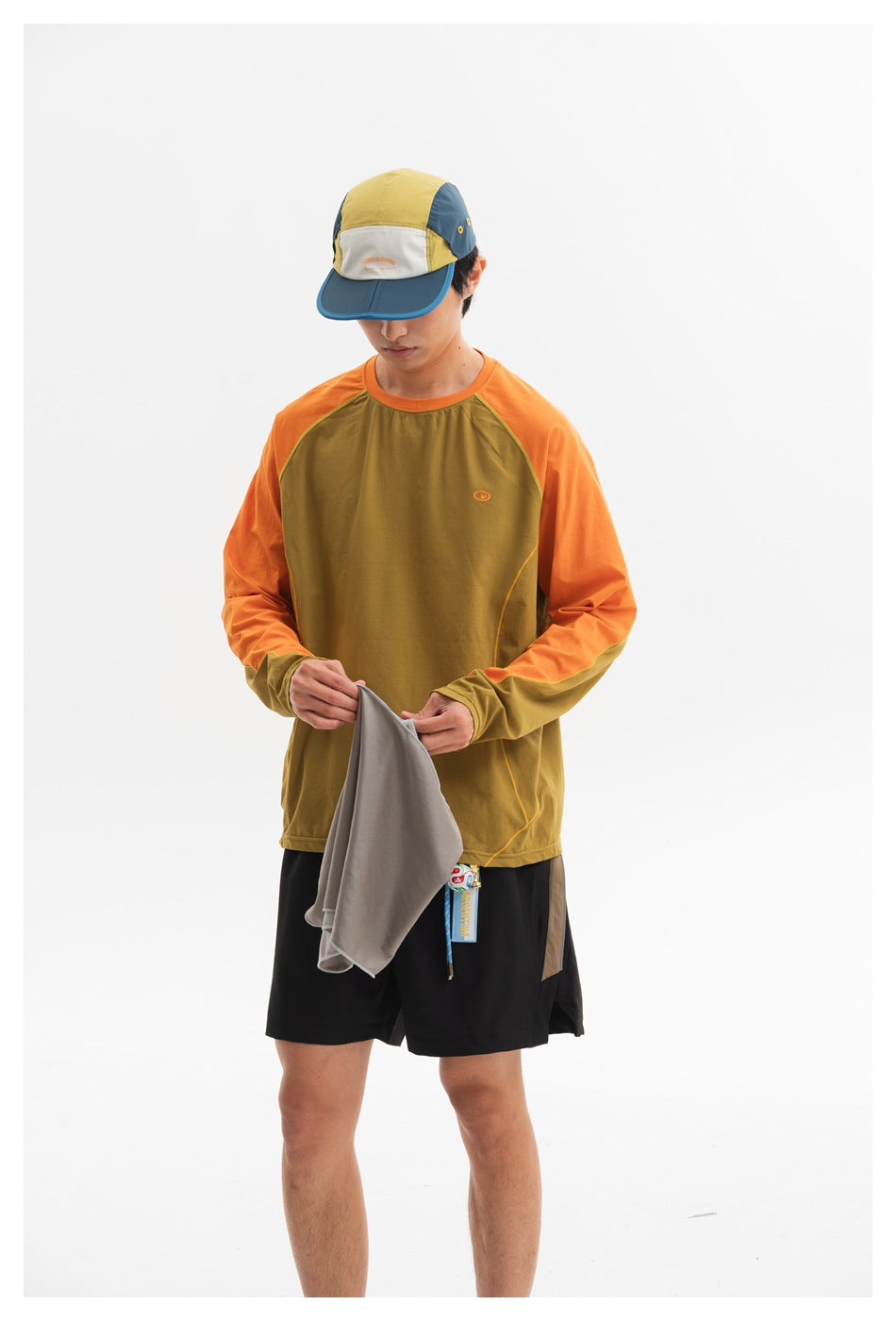 Front view of a model wearing an olive long-sleeve top with orange raglan sleeves and black shorts.