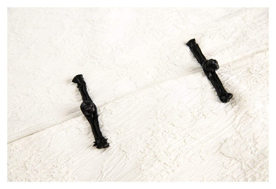 Close-up of textured ivory fabric with two black knotted frog closures.