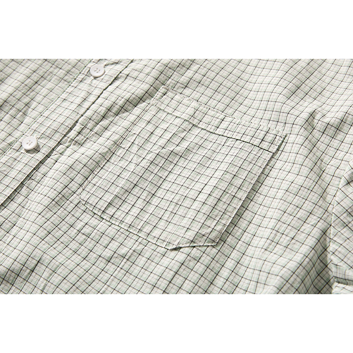Close-up of a square chest pocket on a pale green and gray plaid shirt, with part of the button placket visible.