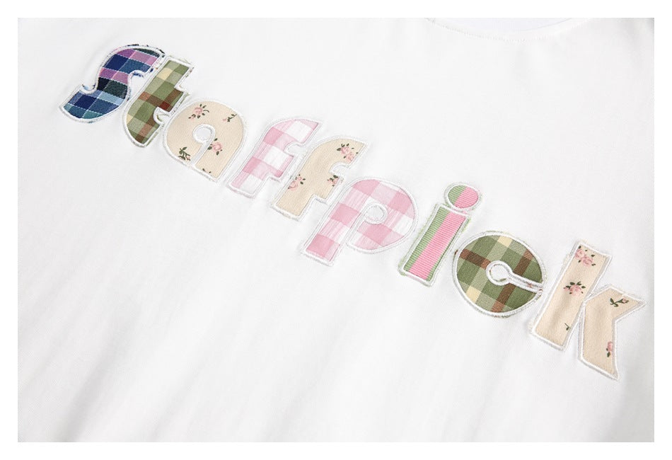 Close-up of colorful patchwork appliqué lettering on a white T-shirt.