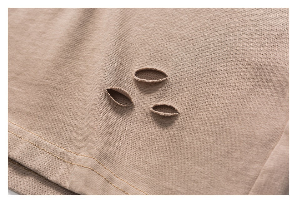 Close-up of three oval distressed cutouts and a stitched hem on taupe T-shirt fabric.