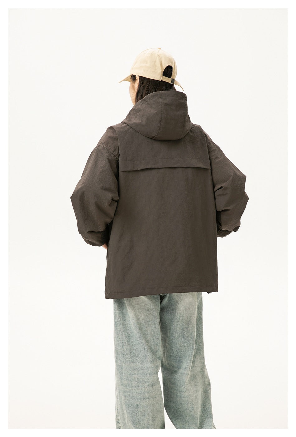 Rear view of a woman wearing a dark charcoal hooded jacket with a back yoke and loose light-wash jeans.