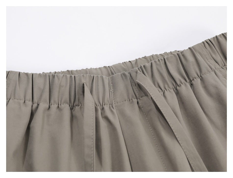 Close-up of taupe trousers with a gathered elastic waistband and two drawstrings.