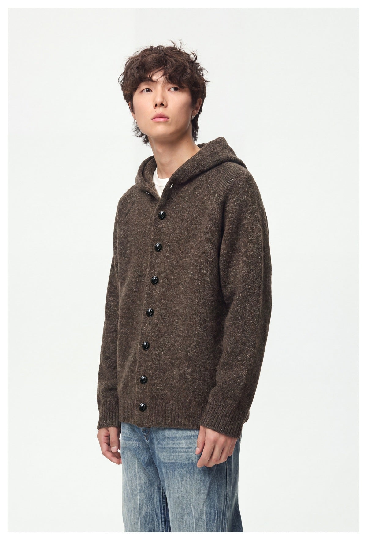 Man in a brown hooded knit button-front jacket and blue jeans, angled three-quarter view