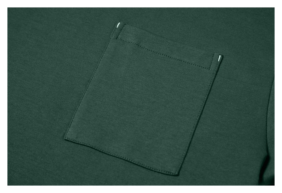 Close-up of a rectangular chest pocket with small light-colored details at its upper corners on dark green fabric.
