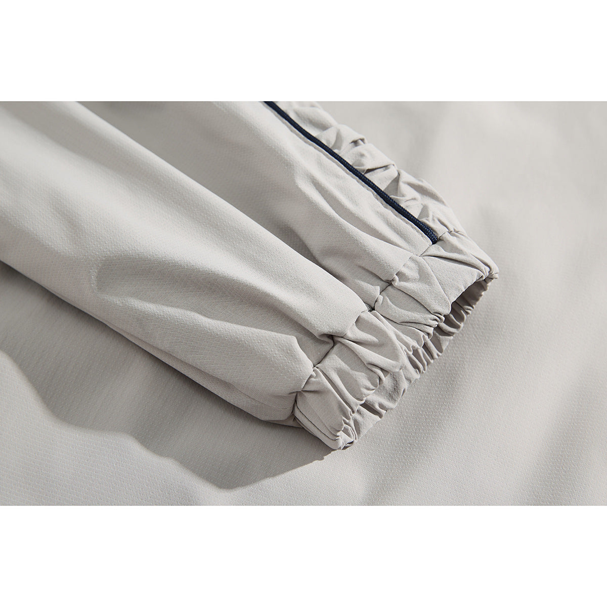 Close-up of a light gray jacket sleeve with a gathered elastic cuff and dark piping.