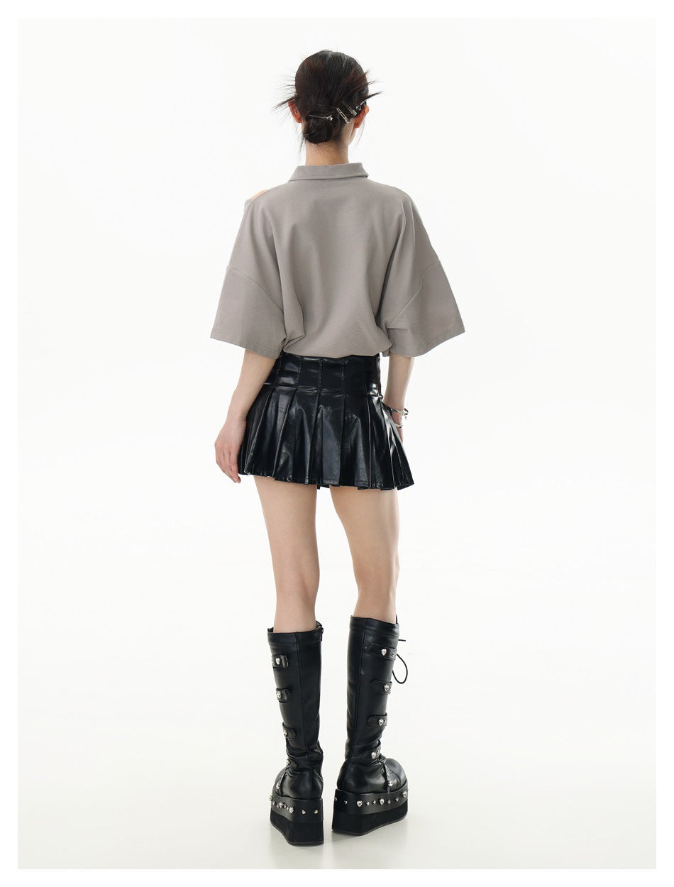 Back view of a model wearing a taupe oversized short-sleeve collared top with a black pleated skirt.