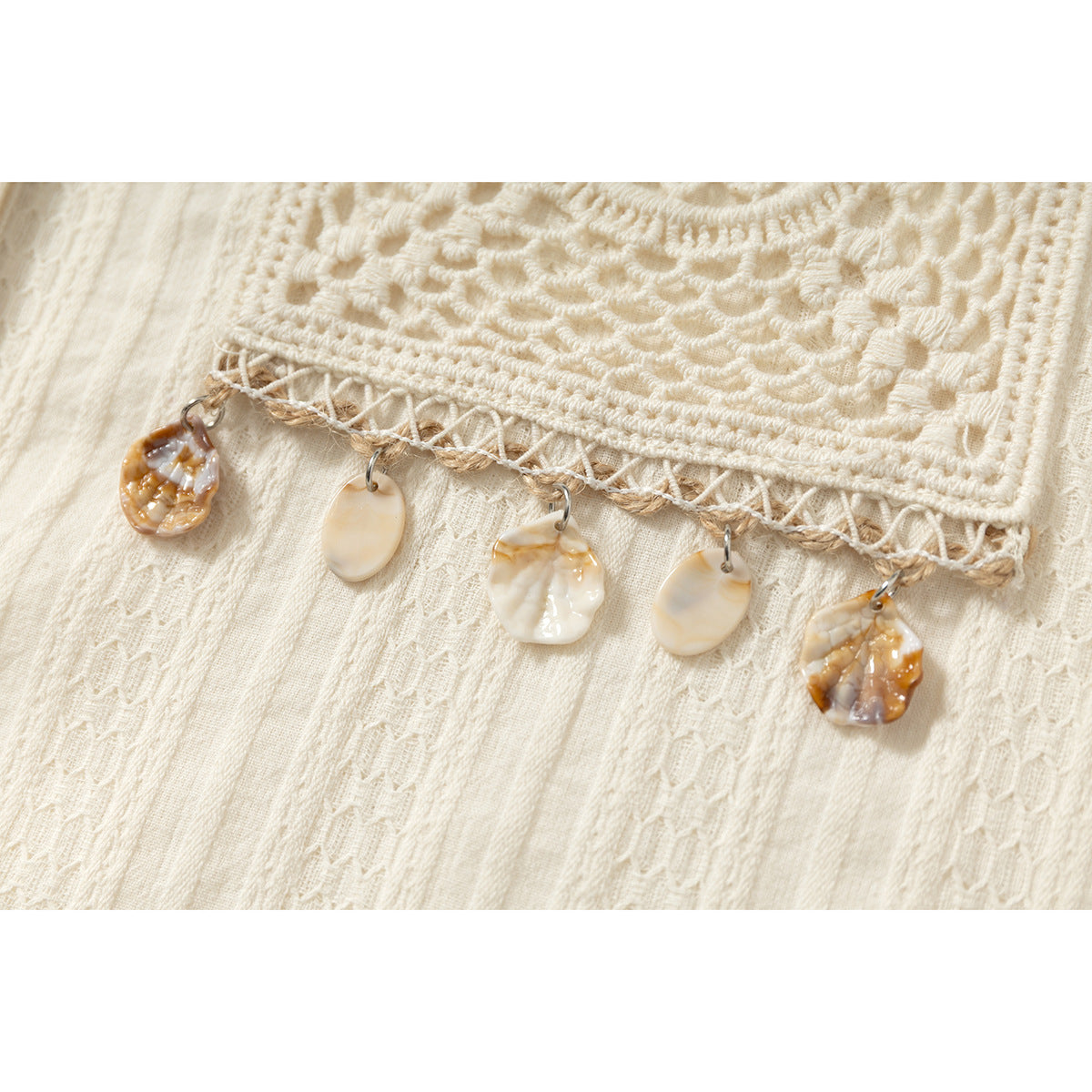 Close-up of an ivory shirt’s crocheted pocket trim with five dangling shell-shaped charms.