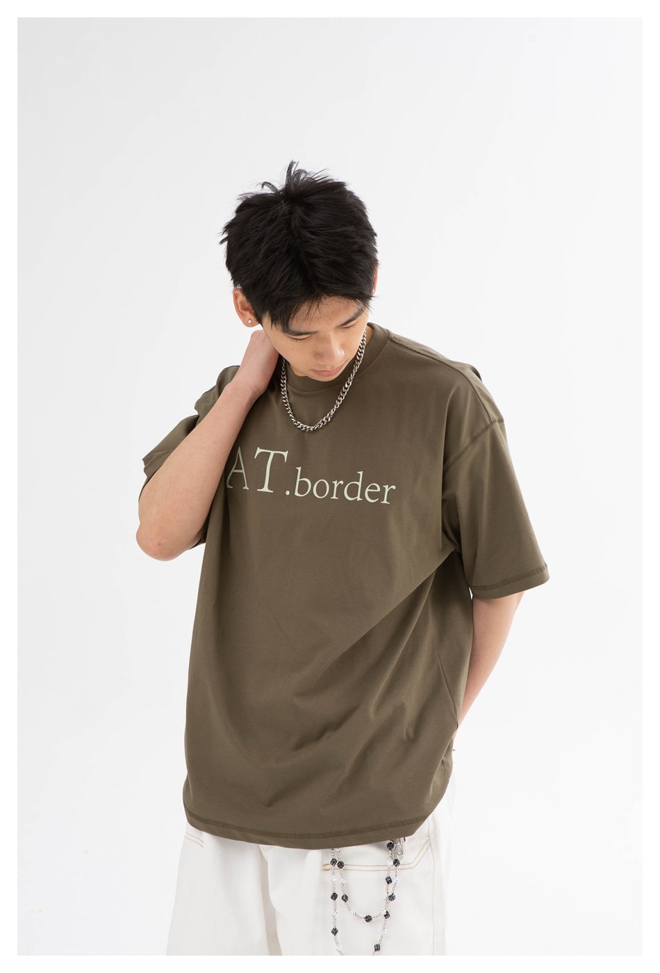 Model wearing an olive-brown oversized T-shirt with pale lettering, shown from the front.