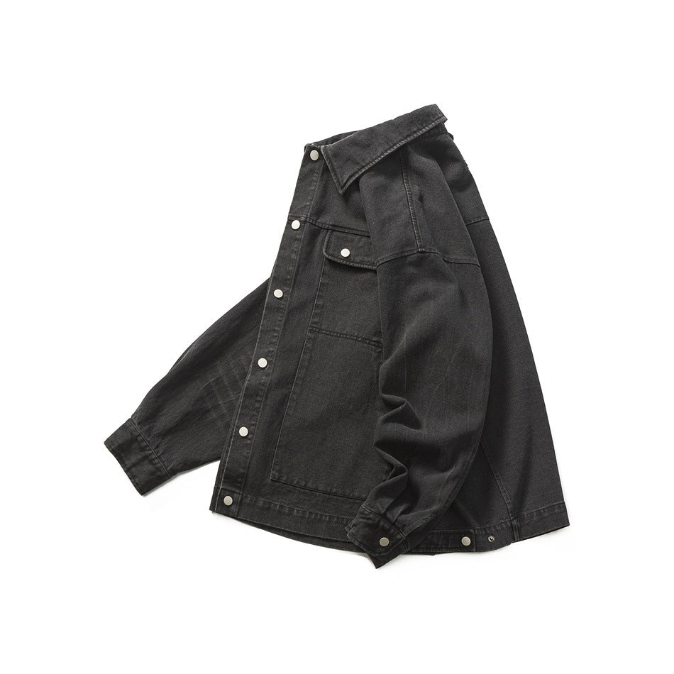 Black denim jacket arranged in a folded, angled front view, with a pointed collar, snap buttons, and chest pocket.