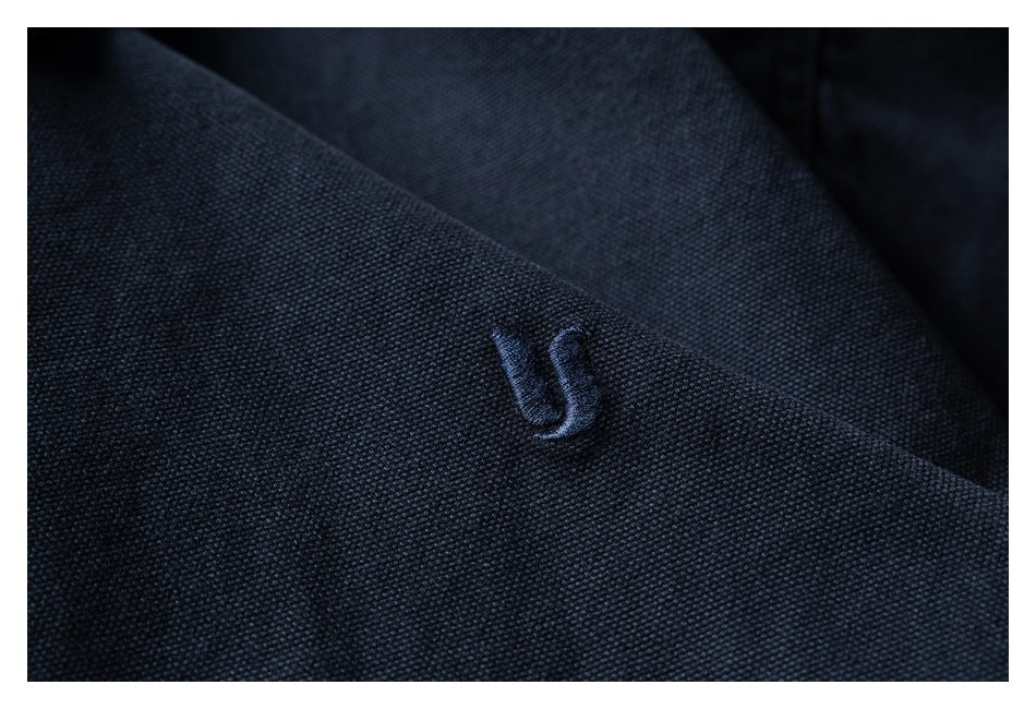 Close-up of a small tonal embroidered emblem on dark navy fabric.