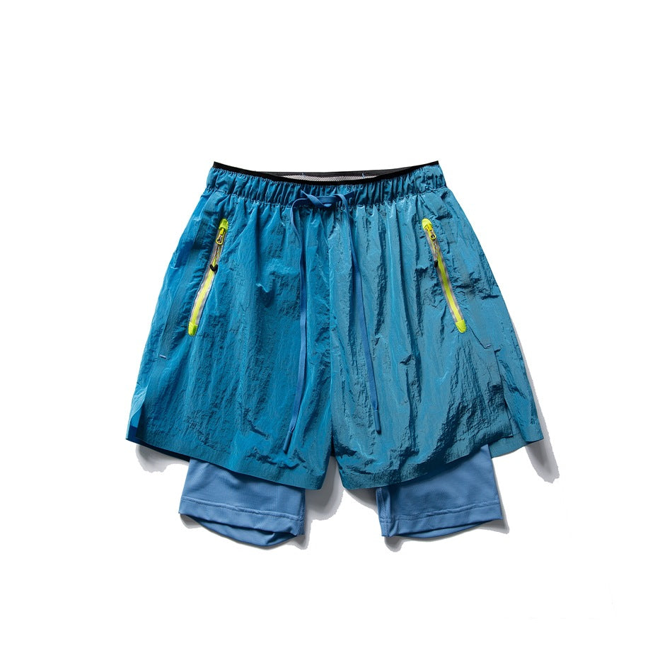 Front view of shiny teal-blue layered shorts with a drawcord and two neon-yellow zip pockets.