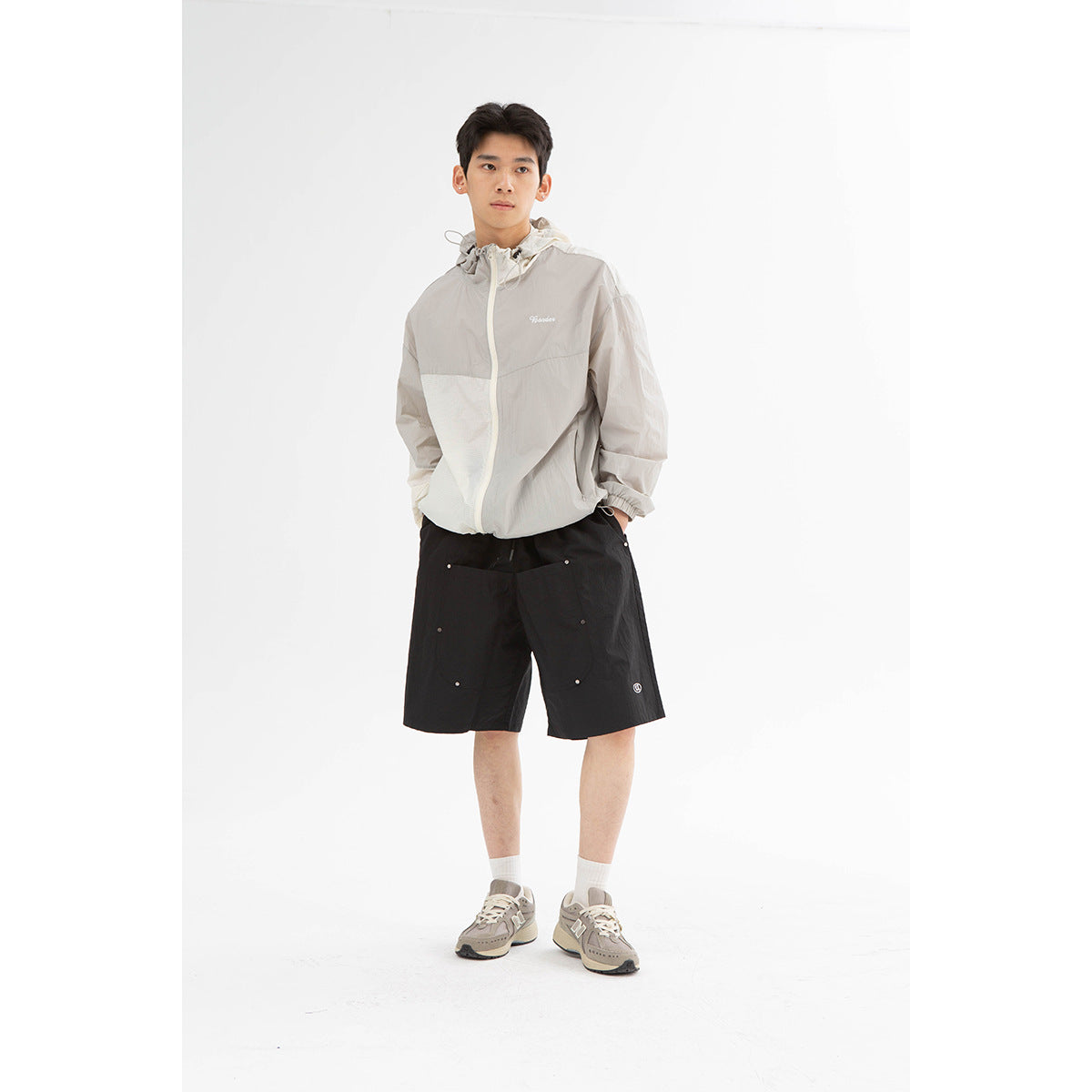 Model wearing a light gray color-block hooded jacket and black utility shorts, shown full length from the front.