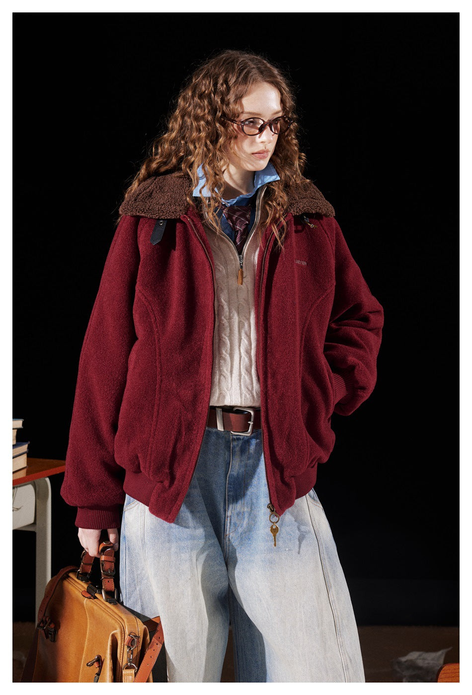 Model wearing a burgundy zip-up jacket with a brown fleece collar, layered over a cream cable-knit sweater.