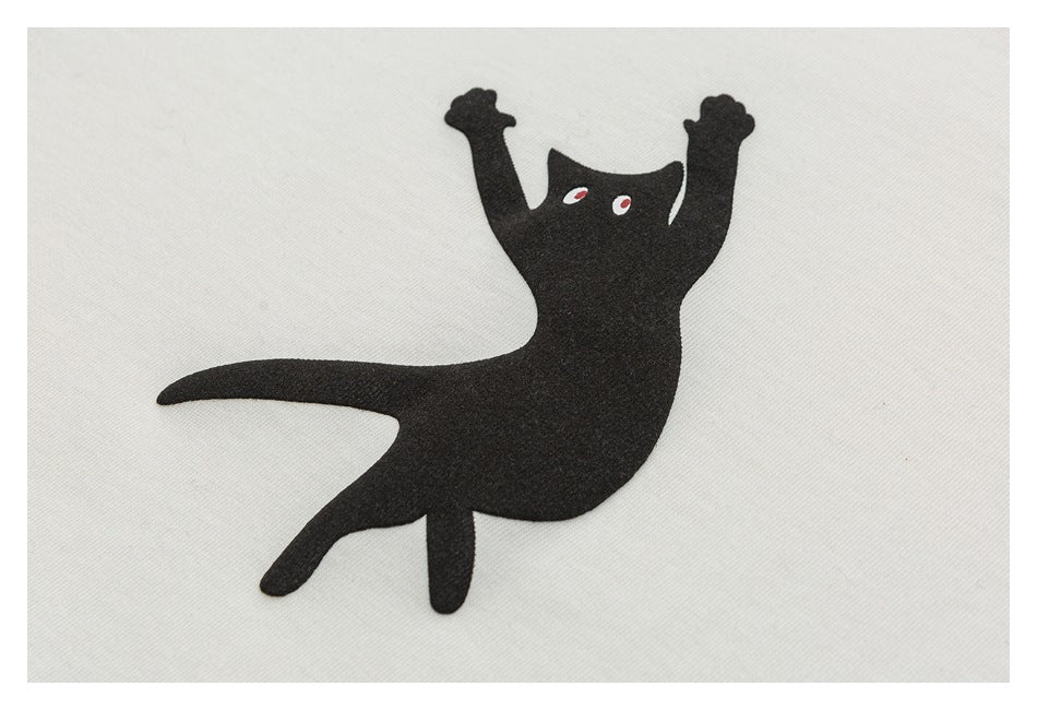 Close-up of a black stylized animal graphic with red-and-white eyes on off-white fabric.