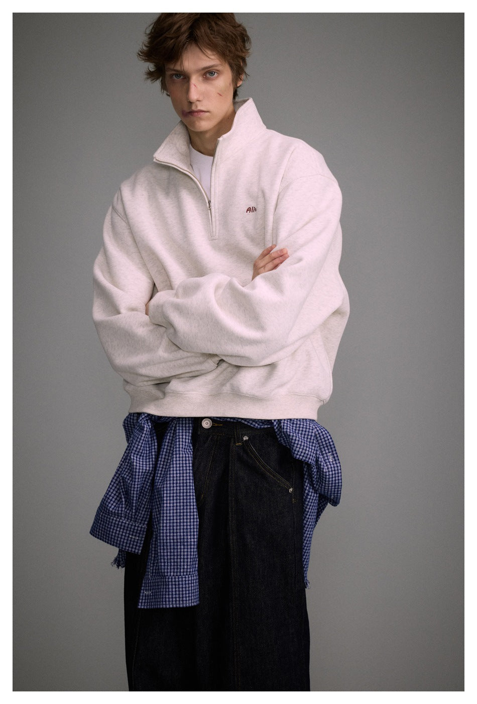 Model wearing a loose light heather quarter-zip sweatshirt with a raised collar and ribbed hem.