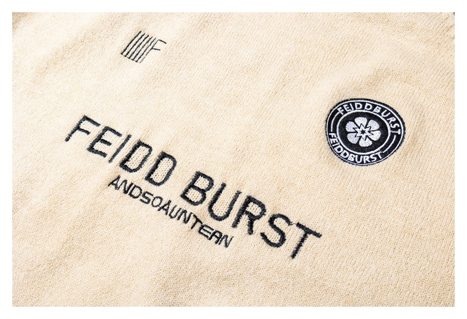 Close-up of black embroidered lettering and a circular emblem on the cream sweater.