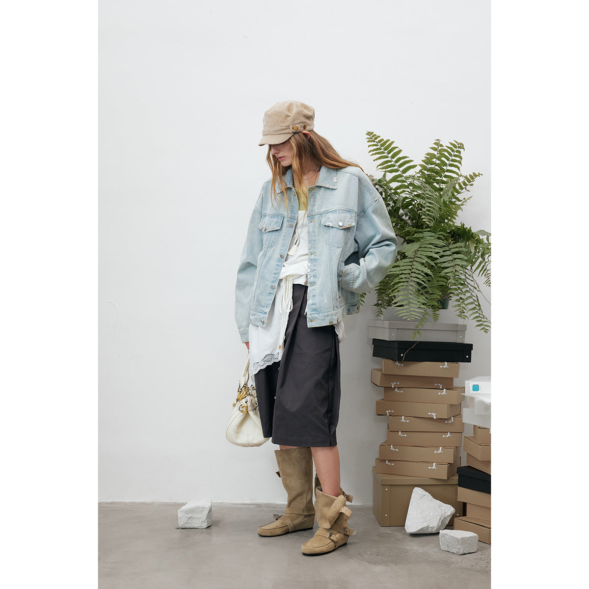 Model wearing an oversized light-wash denim jacket with black shorts, a white lace-trimmed top and tan boots.