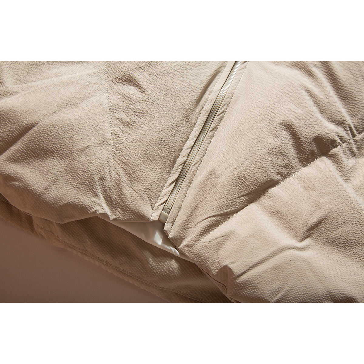 Close-up of the beige jacket's front zipper and textured fabric.