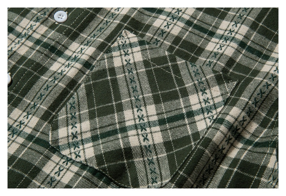 Close-up of the stitched chest pocket on a dark green and cream plaid shirt.