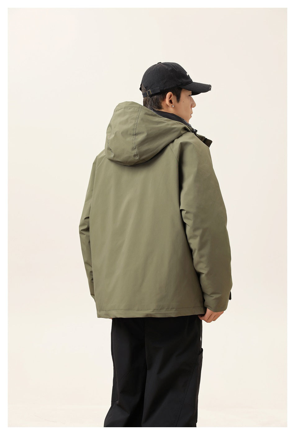 Rear view of a model wearing an olive hooded jacket with black trousers.