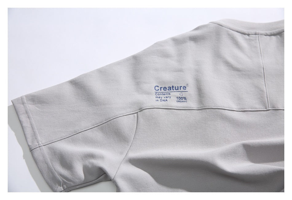 Close-up of the upper back and sleeve of a light gray shirt with a small blue printed design.