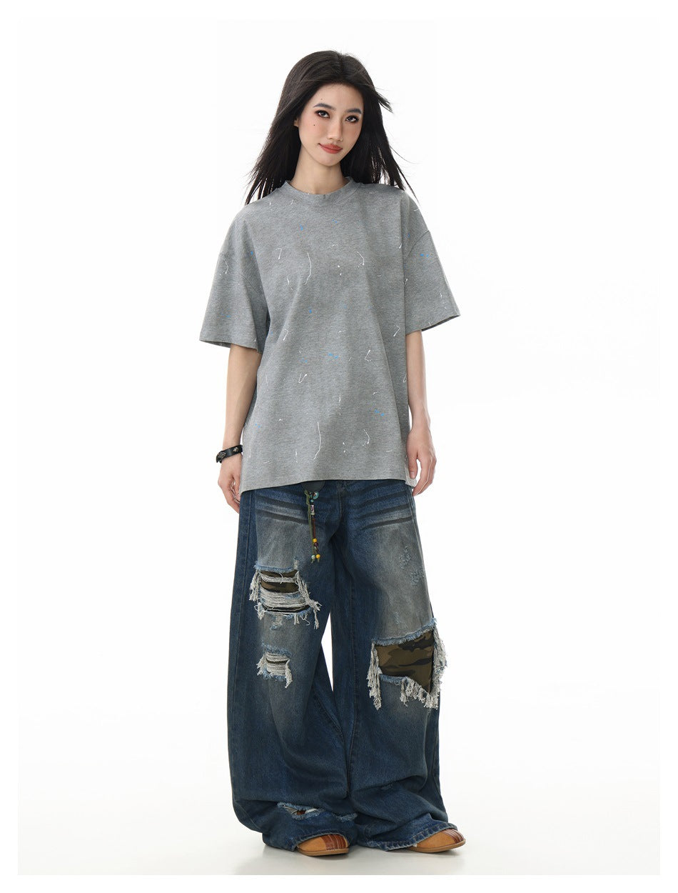 Model wearing an oversized gray short-sleeve T-shirt with scattered blue and white marks and distressed wide-leg jeans.