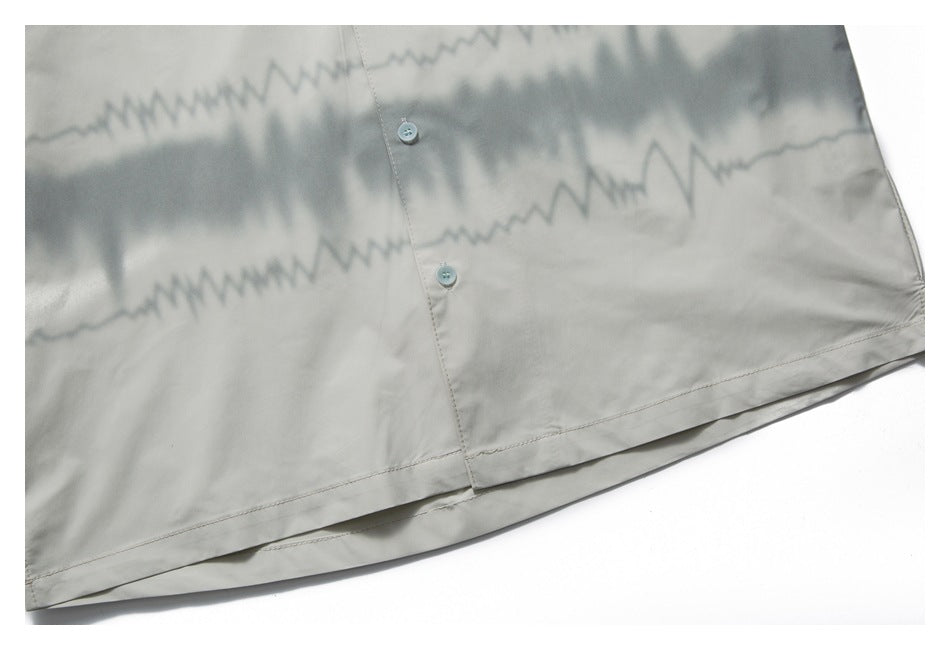 Close-up of a pale gray shirt with a dark jagged pattern, front buttons, and a stitched lower hem.