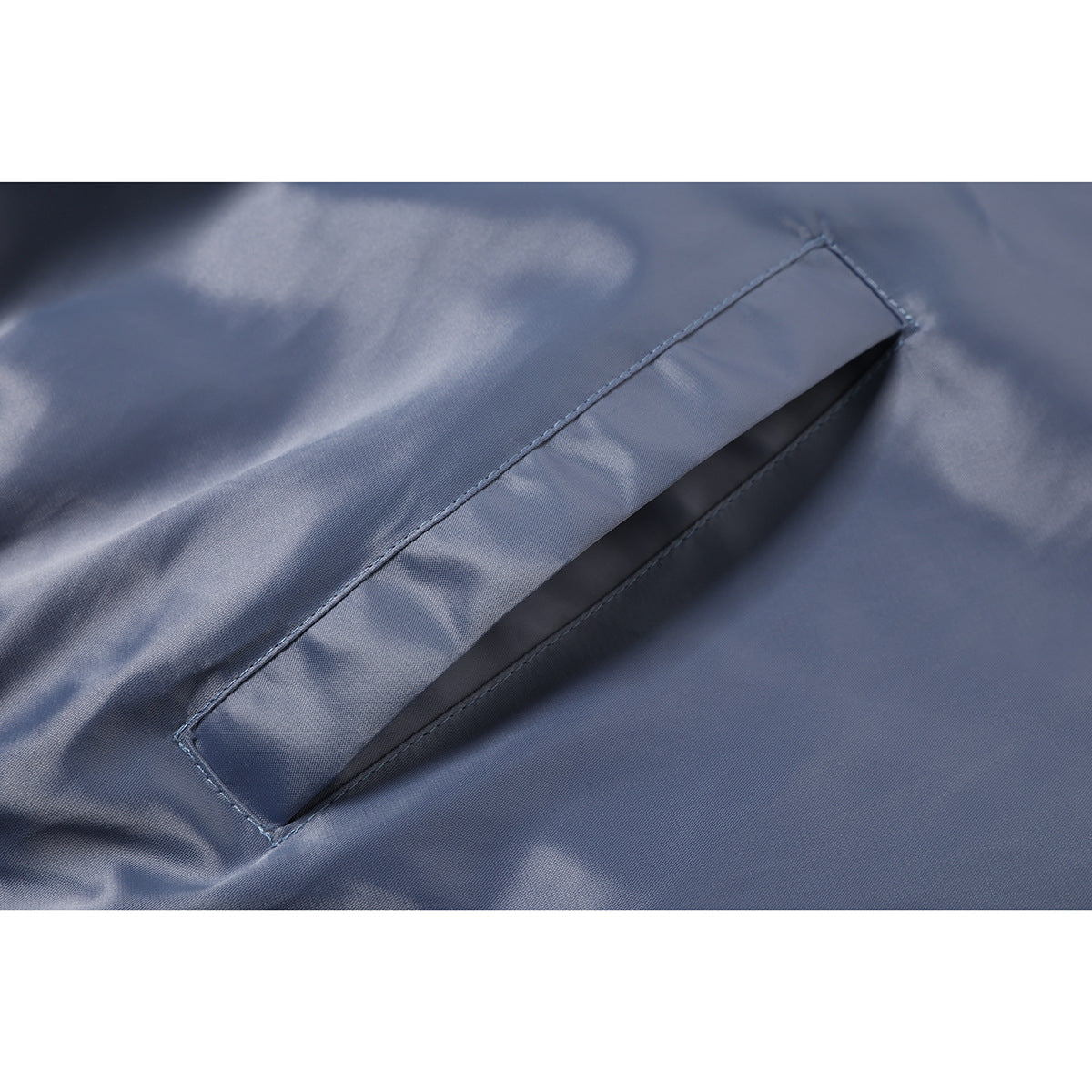 Close-up of a slanted welt pocket and stitching on slate blue jacket fabric.