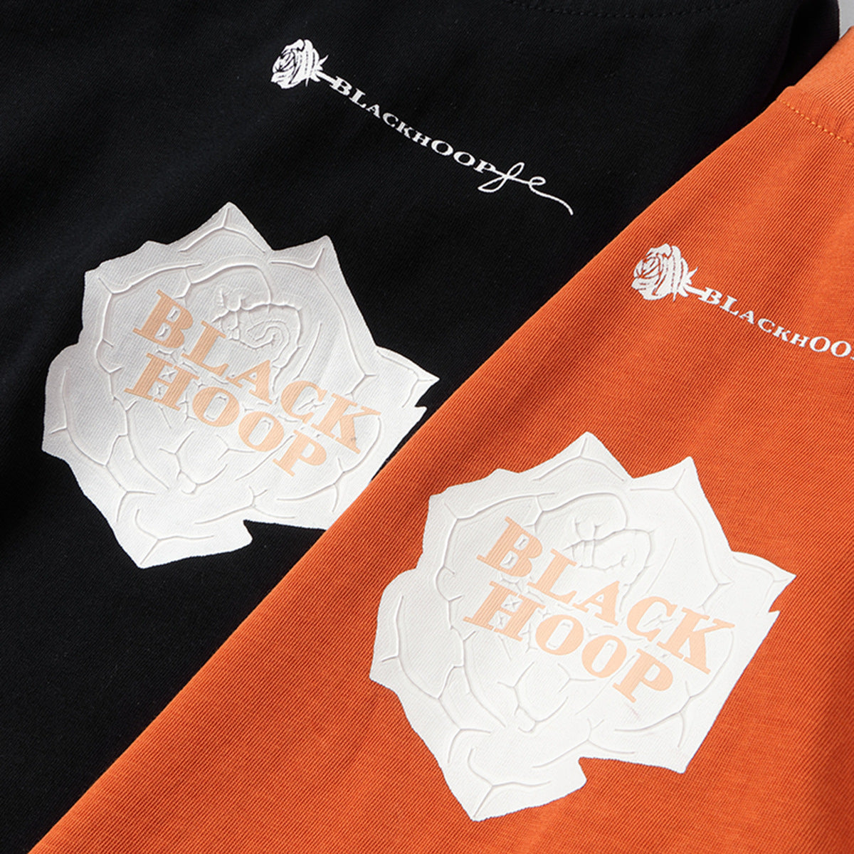 Close-up of orange and black T-shirts with white raised chest graphics and lettering.