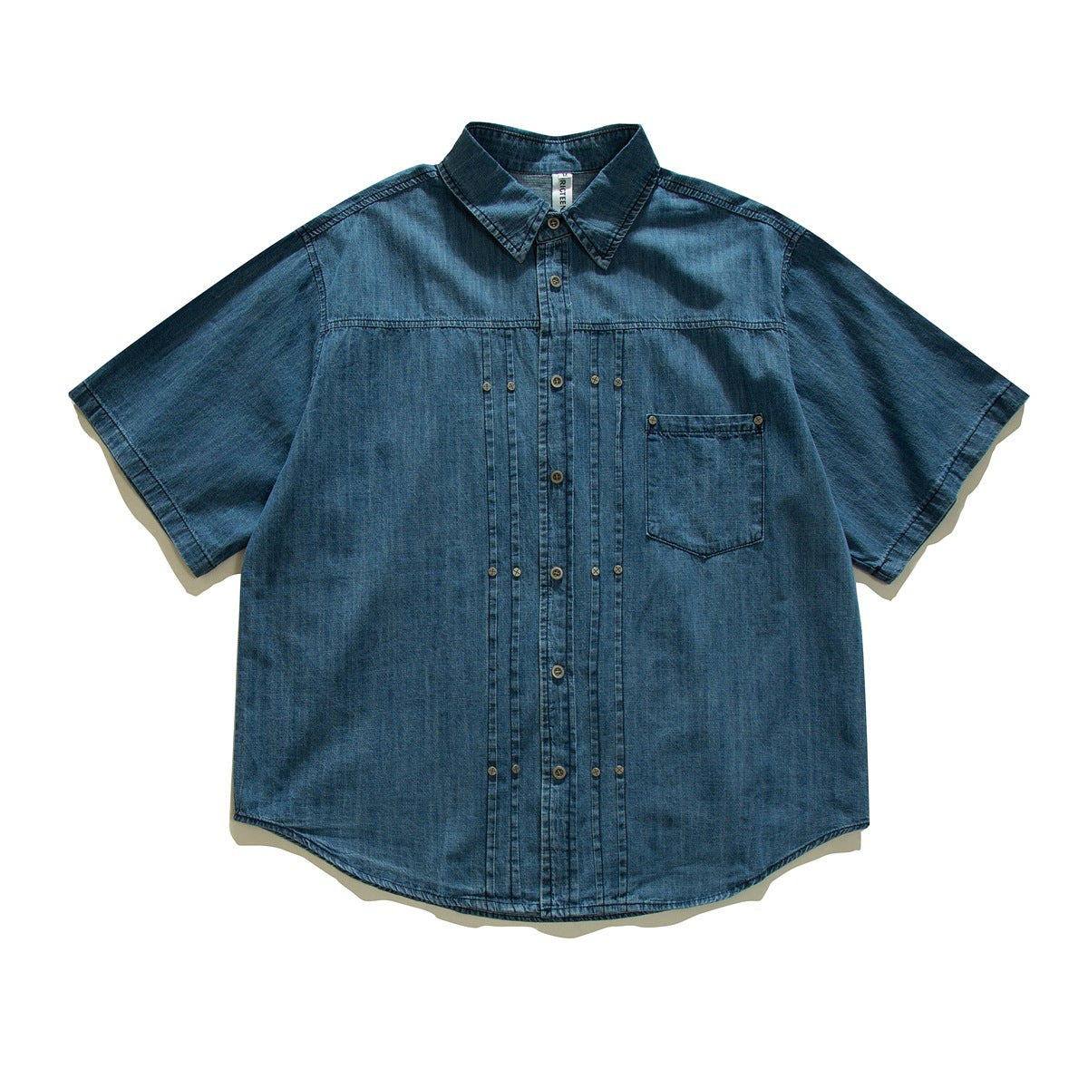 Washed blue short-sleeve denim shirt flat lay with front pleats, rivets, chest pocket and curved hem