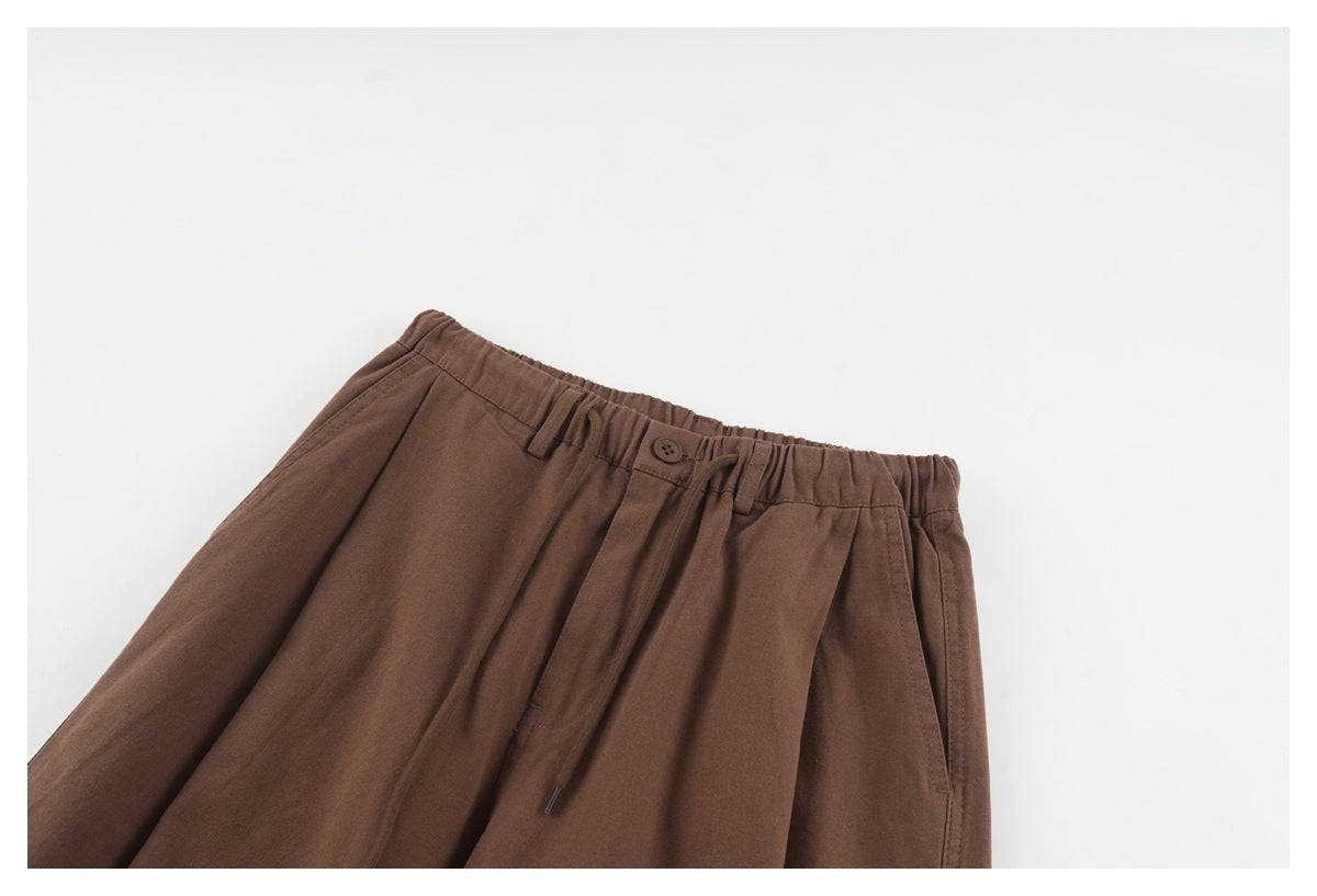 Close-up of brown trousers showing the elasticated waist, button, belt loops, drawstring and side pocket.