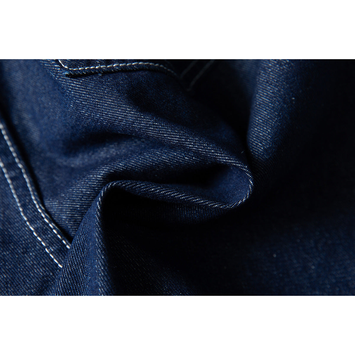 Macro view of dark indigo denim folds and contrasting white stitching.