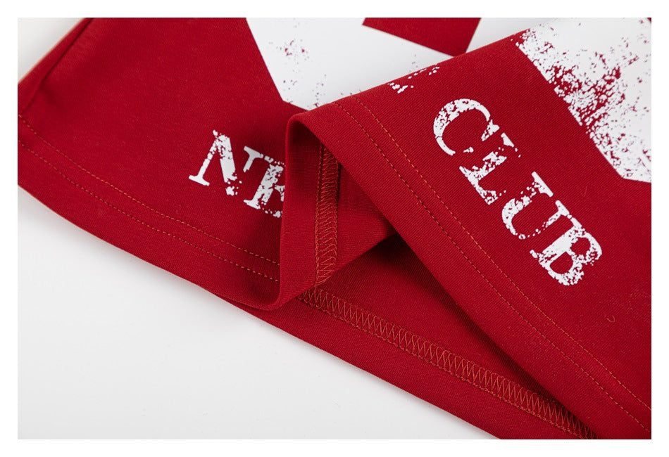 Close-up of a red shirt's folded hem, stitching, and distressed white English print.