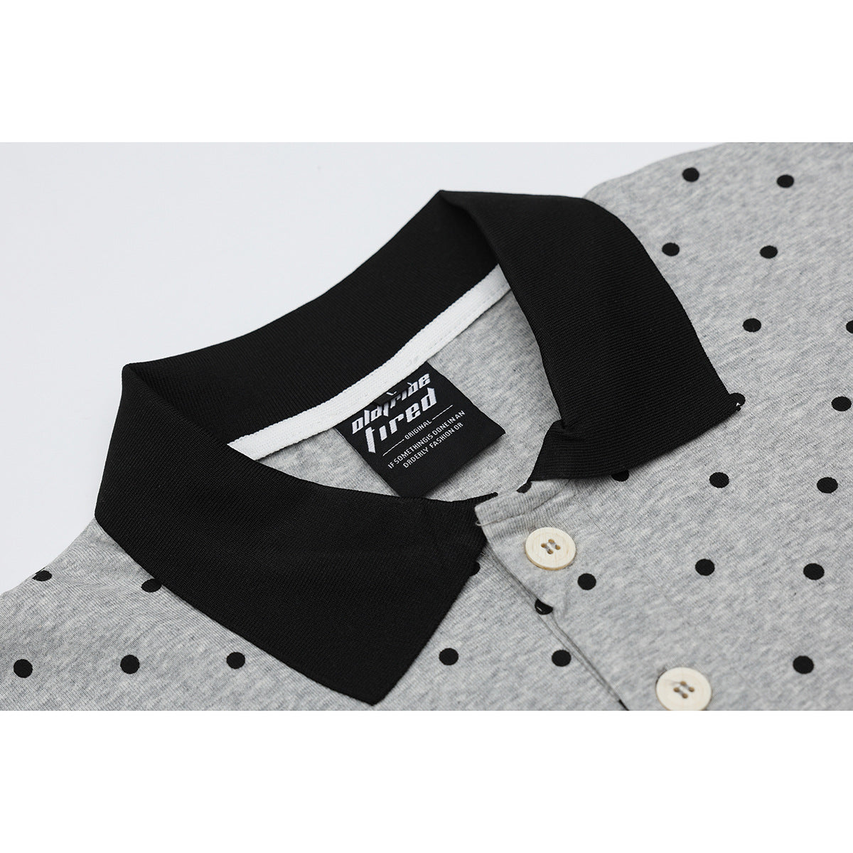 Close-up of a gray heather polo with black polka dots, a black collar, cream buttons and an interior neck label.