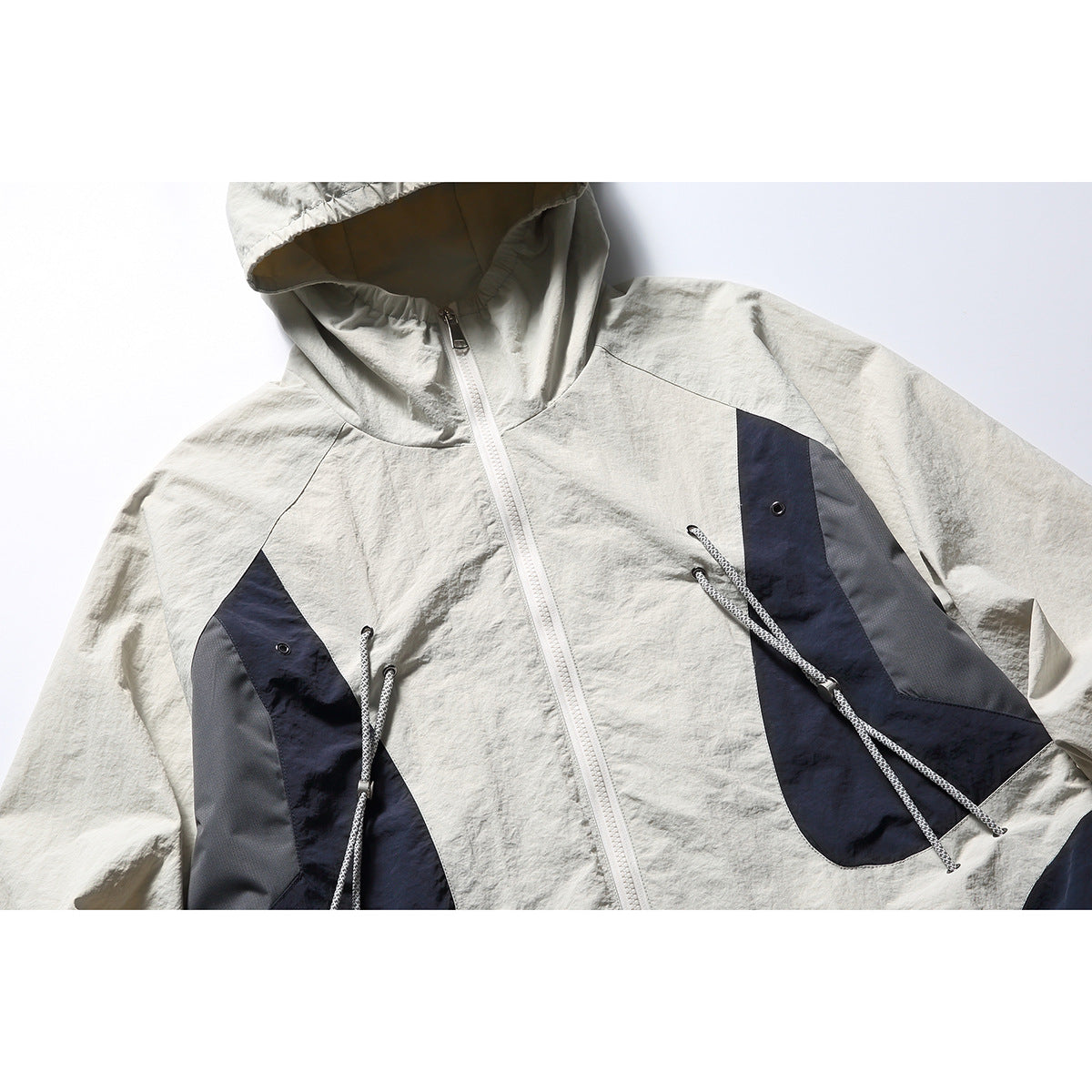 Close-up of an off-white hooded jacket front with a white zipper and navy and gray panels with drawcords.