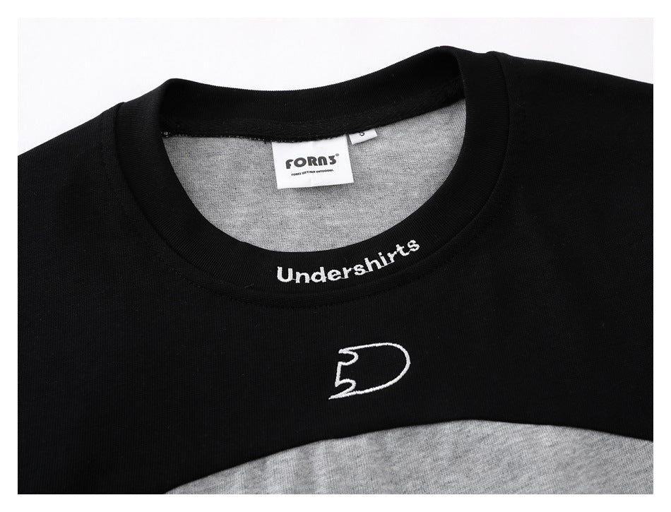 Close-up of a black crew neck and chest with white embroidered lettering and emblem on a gray color-block shirt.