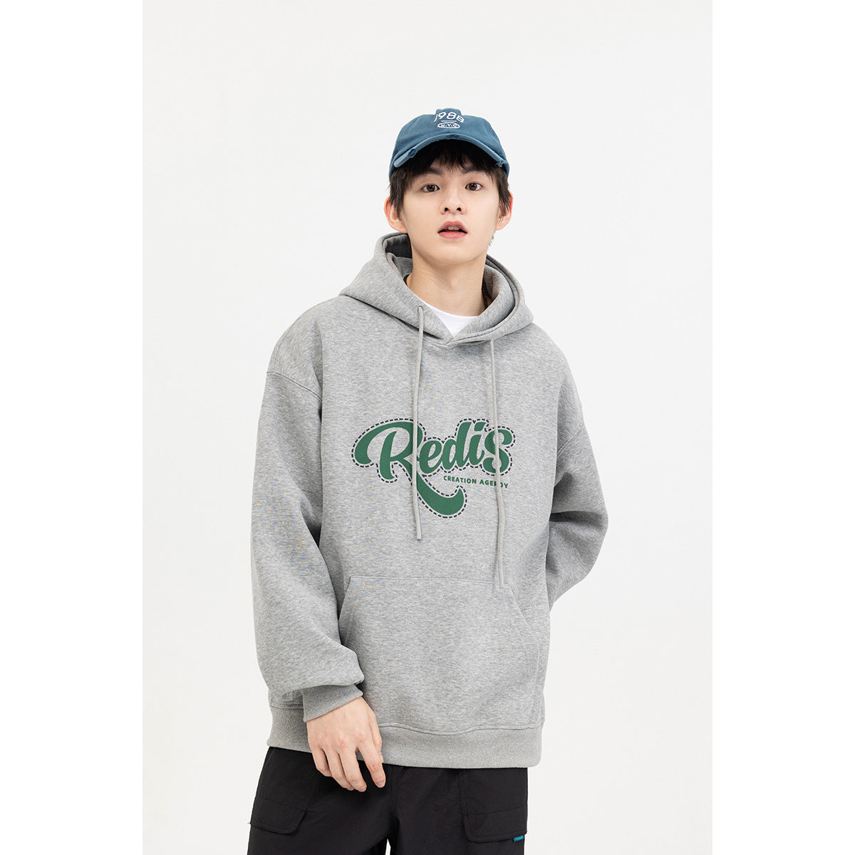 Model wearing a light gray oversized hoodie with drawstrings, a kangaroo pocket, and a large green chest graphic.
