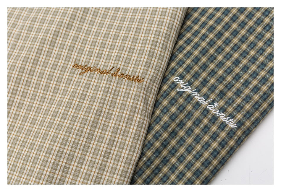 Close-up of cream-and-brown and teal-and-brown plaid shirts with cursive embroidery.