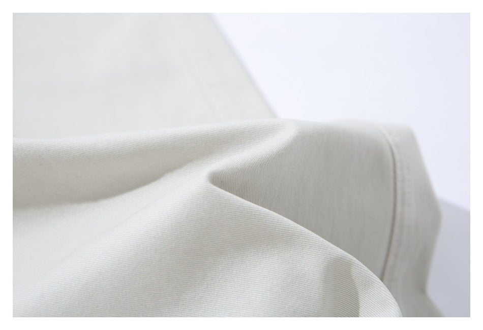 Close-up of the fine diagonal texture and drape of ivory trouser fabric.