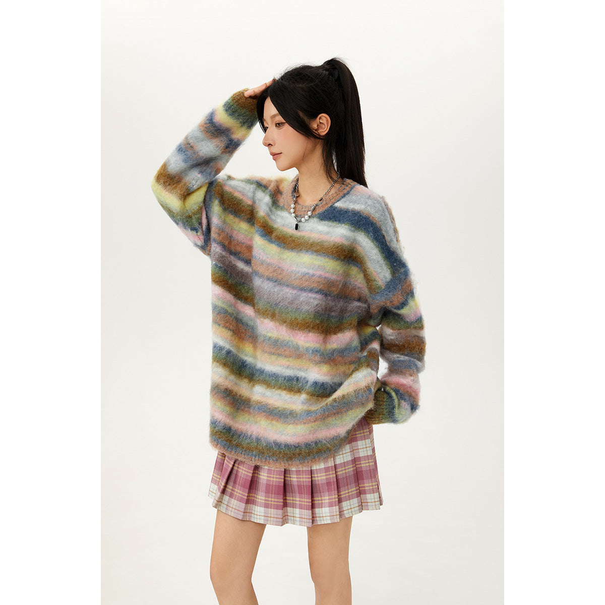 Side view of a model wearing an oversized multicolor striped sweater with a pink plaid pleated skirt.