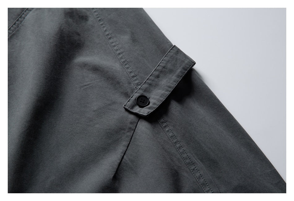 Close-up of dark charcoal pants with a small buttoned tab and stitched panel seams.