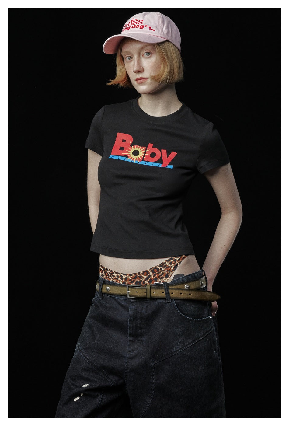 Closer view of a model wearing a black graphic T-shirt, wide black jeans, and a pale pink cap.