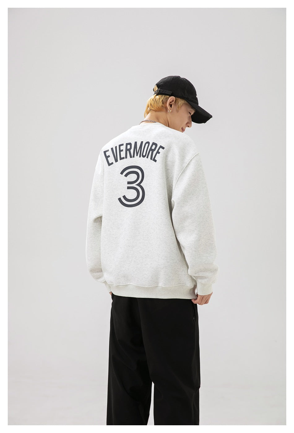 Back view of a model wearing a light gray sweatshirt with dark EVERMORE lettering and a large number 3.
