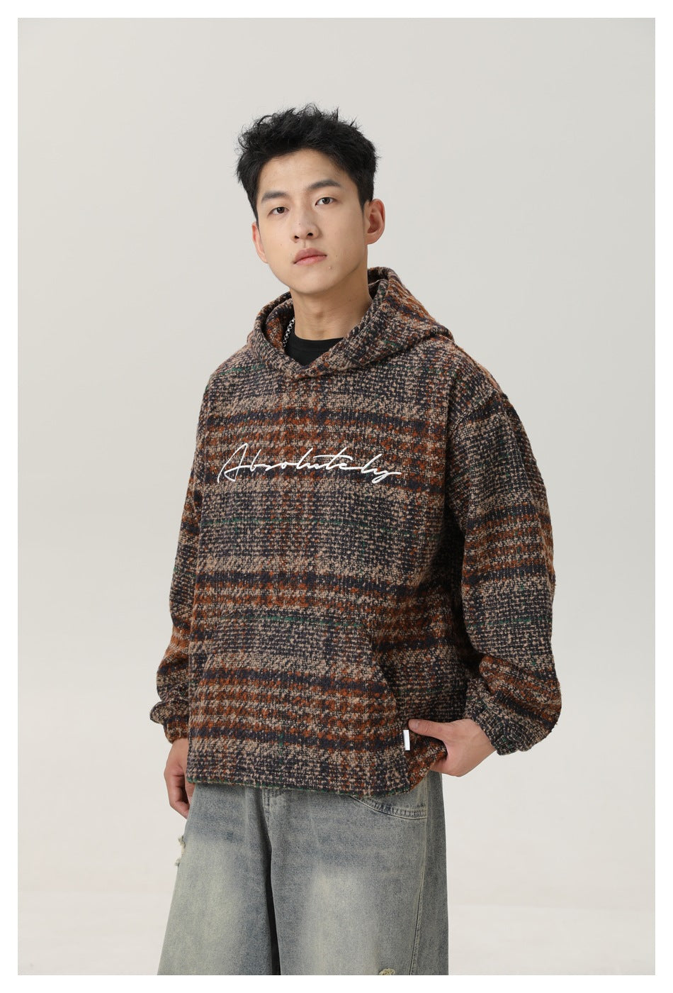 Three-quarter front view of a man wearing a brown, charcoal and beige striped hooded pullover with white script across the