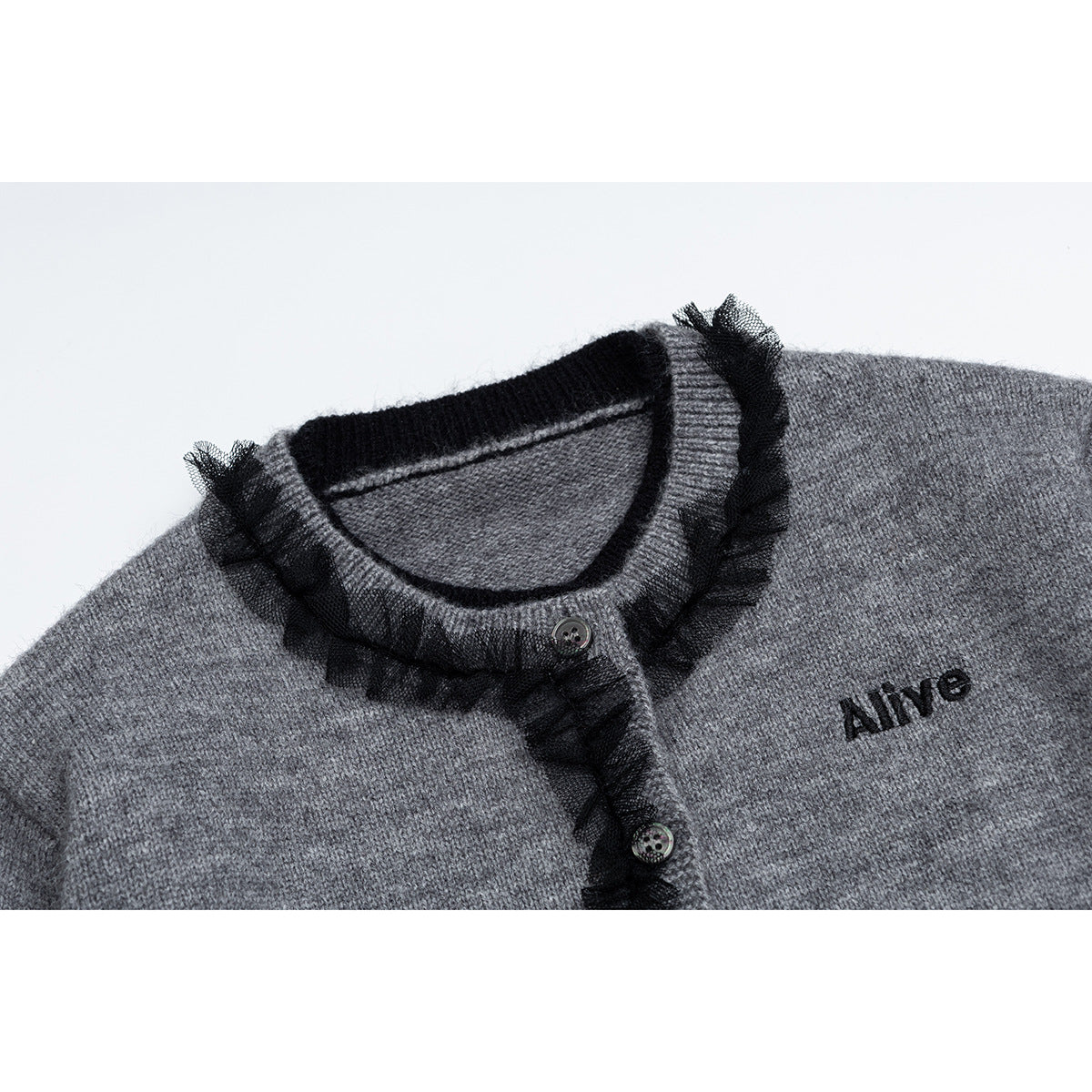 Close-up of a gray knit cardigan neckline with black ruffle trim, buttons, and embroidered “Alive” text.