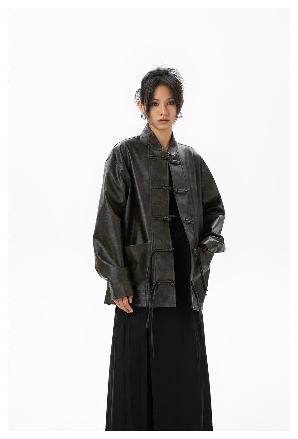 Model wearing the dark brown stand-collar jacket with frog buttons and tassel ties, hand in pocket, over black outfit