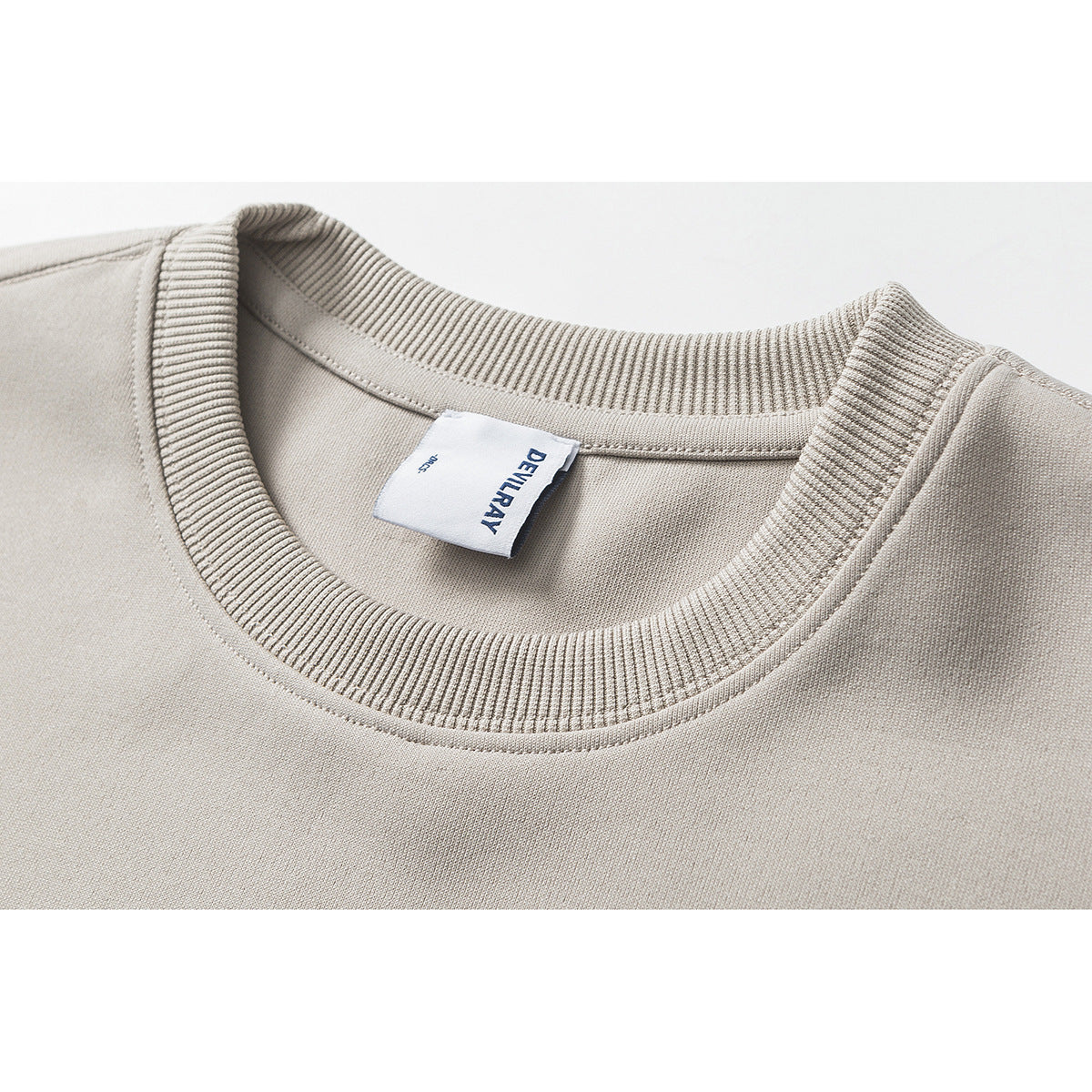 Close-up of a light beige T-shirt neckline with ribbed crew neck and a sewn white label.