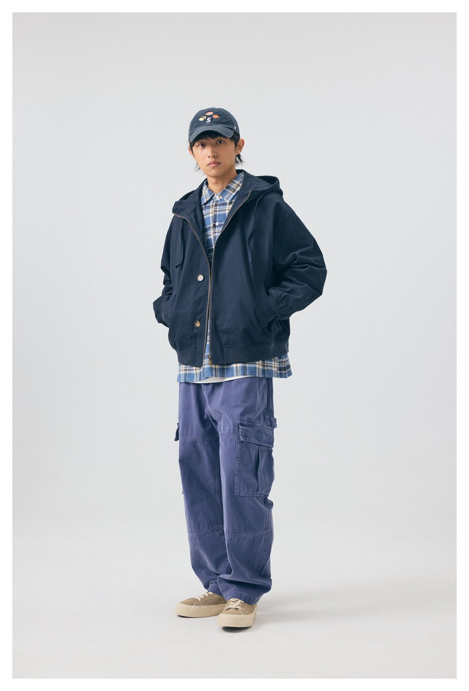 Model wearing navy hooded zip jacket over a plaid shirt with blue cargo pants, front view, hands in pockets
